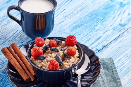 Mug with yogurt and oatmeal porridge with fresh berries and fruit in dark blue bowl on blue wooden background. Concept of healthy lifestyle, healthy food, dieting