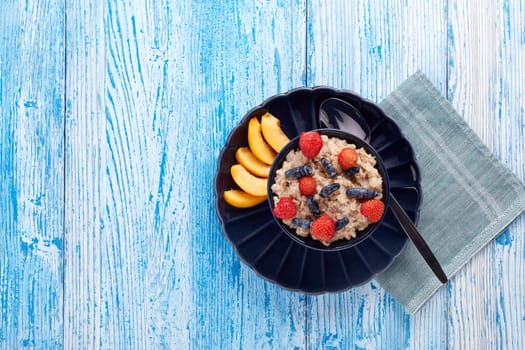 Oatmeal porridge with fresh berries and fruit in dark blue bowl on blue wooden background. Top view with copy space. Concept of healthy lifestyle, healthy food, dieting, vegetarian food