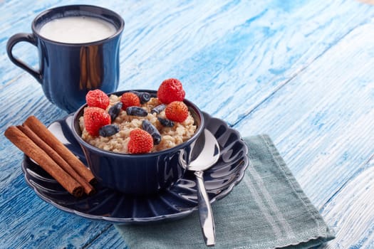 Mug with yogurt and oatmeal porridge with fresh berries and fruit in dark blue bowl on blue wooden background. Concept of healthy lifestyle, healthy food, dieting