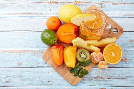 Fruit lemonade with ice, leaves of mint, lemon, pineapple, mango and lime slices standing on blue wooden table. Homemade lemonade with mix fruits. Healthy cool beverage, fruit juice. Top view