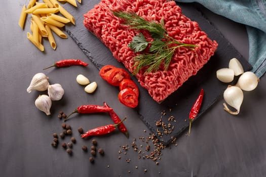 Still life with fresh forcemeat from beef, vegetables, pasta and spices on a dark background. Top view