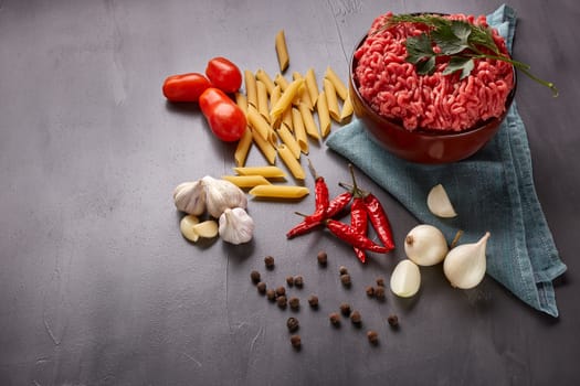 Still life with fresh forcemeat from beef in a bowl, vegetables, pasta and spices on a dark background. Top view