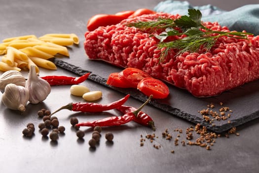 Still life with fresh forcemeat from beef, vegetables, pasta and spices on a dark background.