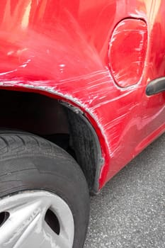 Generic red car with scratched paint and dented body in crash accident or parking lot.