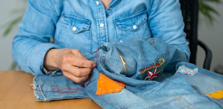 an elderly woman hands sewing on fabric jeans