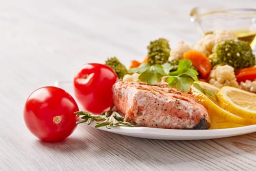 Grilled salmon fillet  garnished with vegetables, lemon, tomato, herbs lying on plate on wooden background. Healthy food. Keto diet.