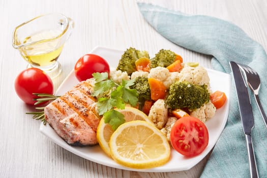 Grilled salmon fillet  garnished with vegetables, lemon, tomato, herbs lying on plate on wooden background. Healthy food. Keto diet.