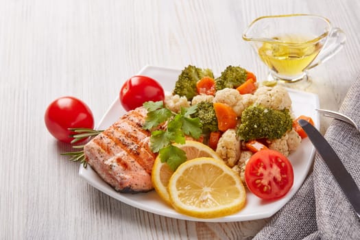 Grilled salmon fillet  garnished with vegetables, lemon, tomato, herbs lying on plate on wooden background. Healthy food. Keto diet.
