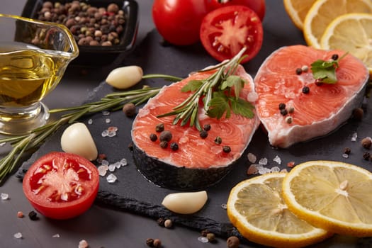 Fresh raw steak of salmon with spices and vegetables lying on stone cutting board on a black background.Top view.Seafood menu