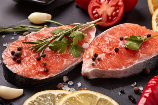 Fresh raw steak of salmon with spices and vegetables lying on stone cutting board on a black background. Seafood menu