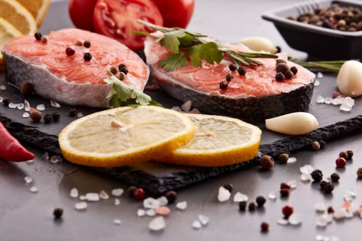 Fresh raw steak of salmon with spices and vegetables lying on stone cutting board on a black background. Seafood menu