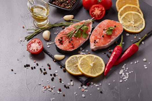 Fresh raw  steak of salmon with spices and vegetables lying on stone cutting board on a black background. Top view. Seafood menu