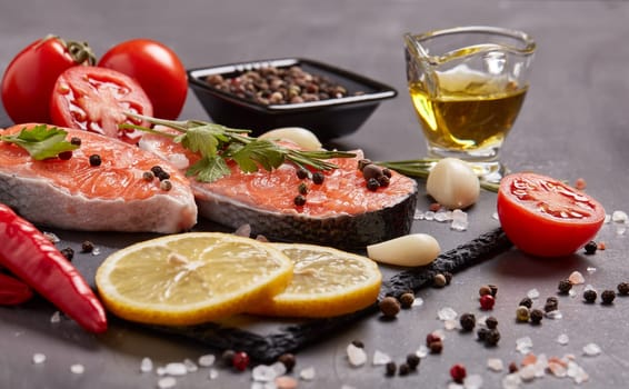 Fresh raw steak of salmon with spices and vegetables lying on stone cutting board on a black background.Top view.Seafood menu