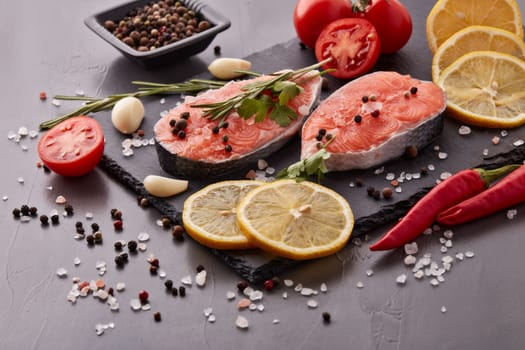 Fresh raw steak of salmon with spices and vegetables lying on stone cutting board on a black background. Seafood menu