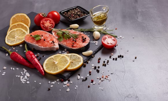 Fresh raw  steak of salmon with spices and vegetables lying on stone cutting board on a black background. Top view with copy space. Seafood menu