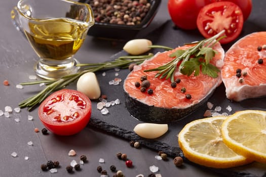 Fresh raw steak of salmon with spices and vegetables lying on stone cutting board on a black background.Top view.Seafood menu