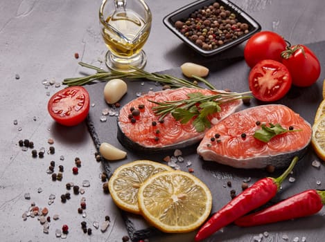 Fresh raw steak of salmon with spices and vegetables lying on stone cutting board on a black background.Top view.Seafood menu