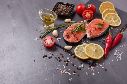Fresh raw  steak of salmon with spices and vegetables lying on stone cutting board on a black background. Top view with copy space. Seafood menu