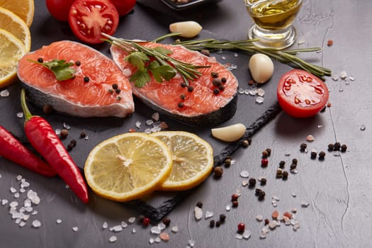 Fresh raw steak of salmon with spices and vegetables lying on stone cutting board on a black background. Seafood menu