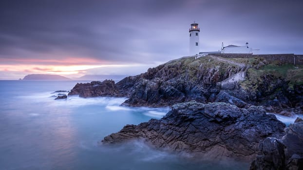 Twilight yields to dawn, sunrise at Fanad Head Lighthouse with blurred water of Atlantic Ocean. Wild Atlantic Way, Donegal, Ireland