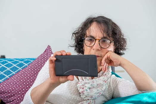 cheerful brunette senior woman using a smartphone while sitting on sofa
