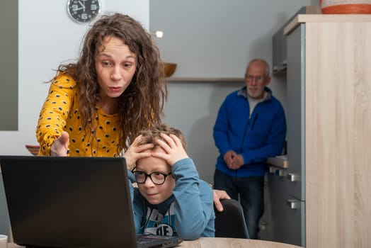 young mother and son using laptop in kitchen for homework