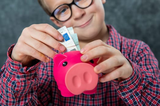 Smile young boy with glasses puts money into a piggy bank