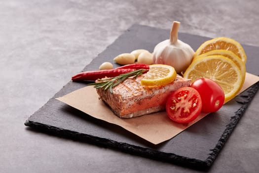 Grilled salmon fillet with spices and vegetables lying on stone cutting board on a grey background. Seafood menu.  Keto diet.