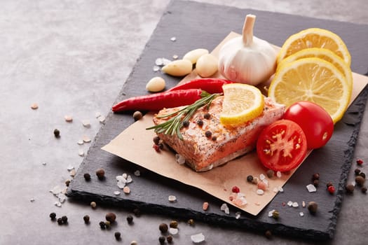 Grilled salmon fillet with spices and vegetables lying on stone cutting board on a grey background. Seafood menu.  Keto diet.