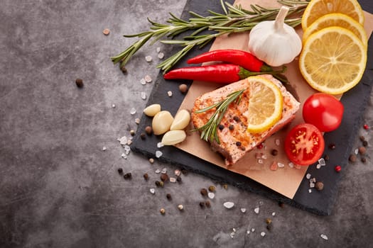 Grilled salmon fillet with spices and vegetables lying on stone cutting board on a grey background. Top view. Seafood menu.  Keto diet.