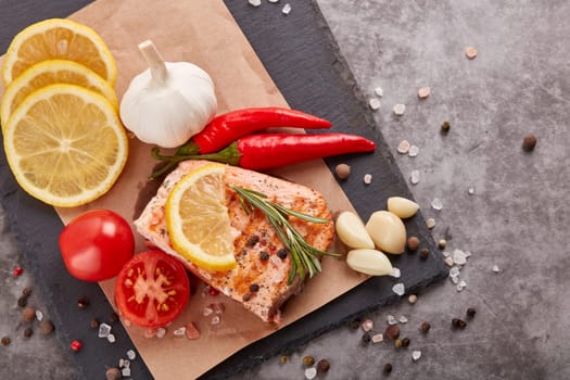 Grilled salmon fillet with spices and vegetables lying on stone cutting board on a grey background. Top view. Seafood menu.  Keto diet.