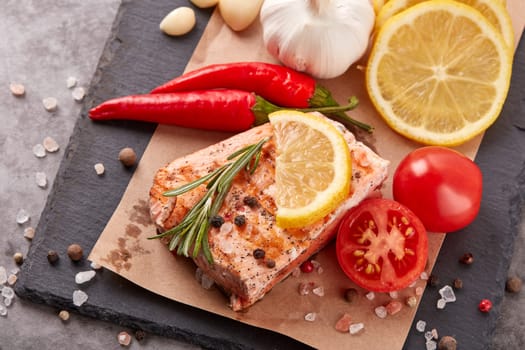 Grilled salmon fillet with spices and vegetables lying on stone cutting board on a grey background. Top view. Seafood menu.  Keto diet.