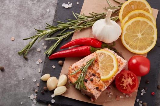 Grilled salmon fillet with spices and vegetables lying on stone cutting board on a grey background. Top view. Seafood menu.  Keto diet.