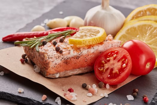 Grilled salmon fillet with spices and vegetables lying on stone cutting board on a grey background. Seafood menu.  Keto diet.