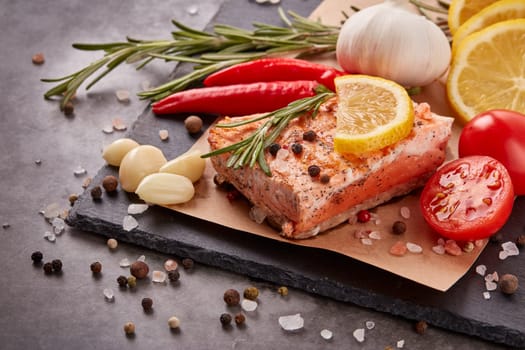 Grilled salmon fillet with spices and vegetables lying on stone cutting board on a grey background. Seafood menu.  Keto diet.