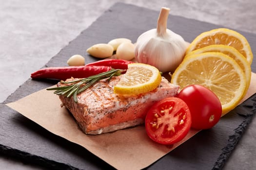 Grilled salmon fillet with spices and vegetables lying on stone cutting board on a grey background. Seafood menu.  Keto diet.