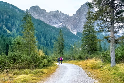 Hiking trip, Dolomites landscape. Pair of tourists is walking along a wide trail in the Dolomites. The Tofane Group in the Dolomites, Italy, Europe.