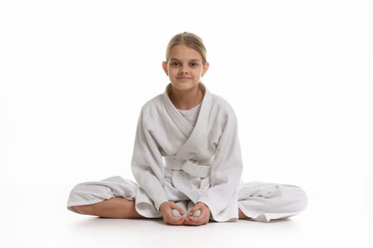 Sporting girl in keikogi sits on the floor, white background