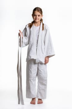The girl stands in a dogi sports fighting dress, and holds her belt in her hands