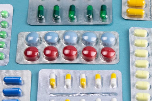Pills of different colours lay on blue background. Colorful antibacterials pills, capsules of medicine.