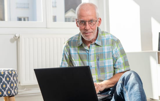 senior man sitting on floor and using a laptop