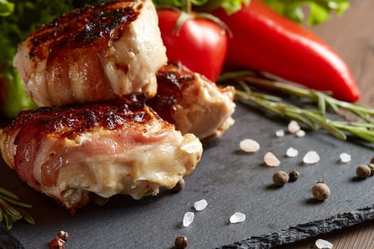 Bacon-wrapped grilled chicken (turkey)  fillet with fresh vegetables and spices on stone cutting board on wooden background