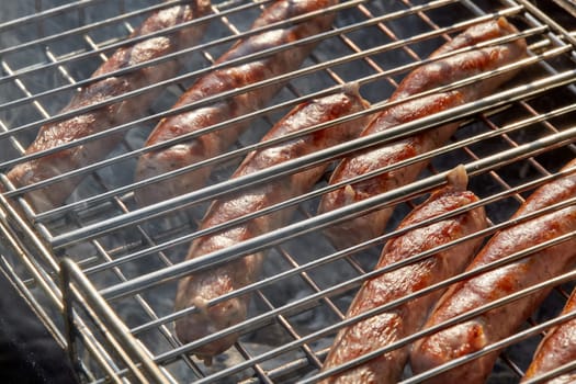 Pork sausages.  Cooking on barbecue grill ( chargrill, brazier). Top view, closeup. Outdoors. Fast food