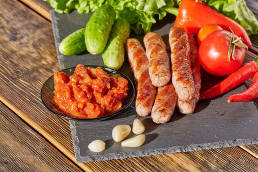 Grilled pork sausages  with fresh vegetables  on stone cutting board on wooden background.