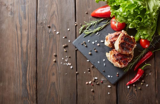 Bacon-wrapped grilled chicken (turkey)  fillet with fresh vegetables and spices on stone cutting board on wooden background. Top view with copy space