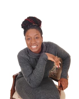 A happy smiling African American woman sitting in a gray dress in an .old armchair, looking into the camera, isolated for white background.