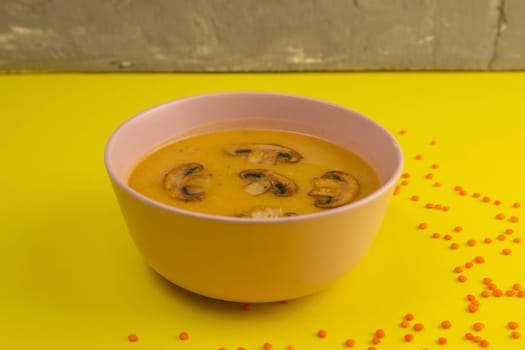 Pea soup with croutons and mushroom on a colored towel that stands on a yellow table.