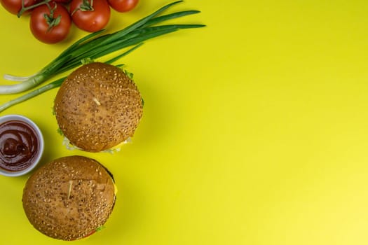 Two hamburgers close-up on a round wooden board, next to, tomatoes, chopped onions and spinach leaves.