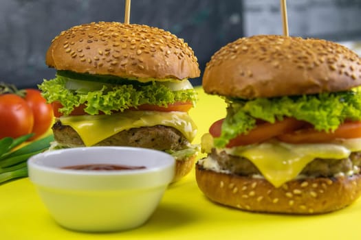 Two hamburgers close-up on a round wooden board, next to, tomatoes, chopped onions and spinach leaves.