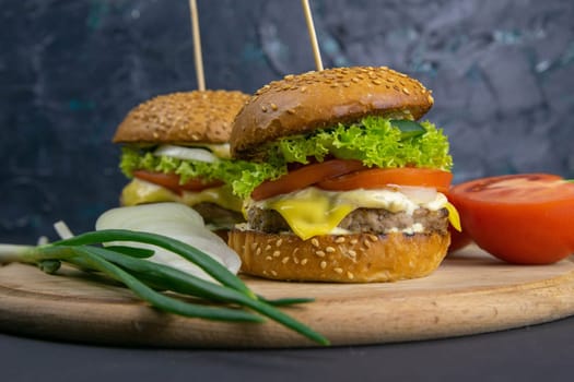 Two hamburgers close-up on a round wooden board, next to, tomatoes, chopped onions and spinach leaves. Top views with clear space